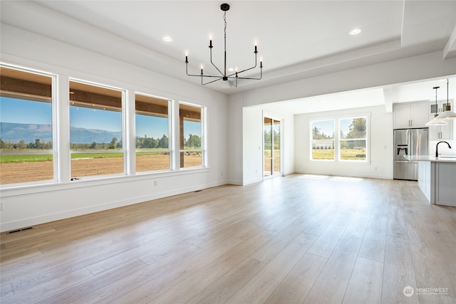 unfurnished living room featuring sink, an inviting chandelier, light hardwood / wood-style floors, and a mountain view