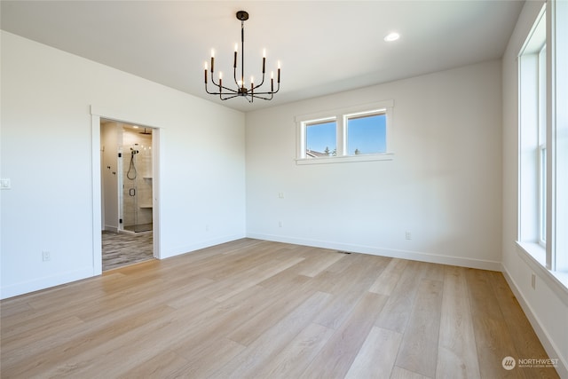 spare room with plenty of natural light, a chandelier, and light hardwood / wood-style floors