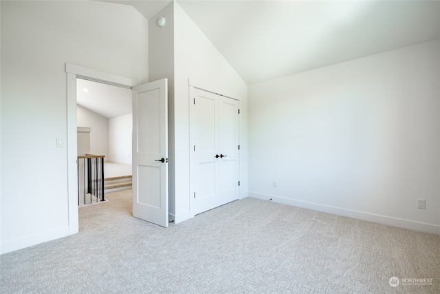 unfurnished bedroom with high vaulted ceiling, a closet, and light colored carpet