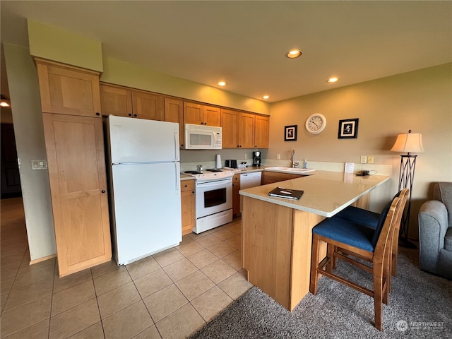 kitchen featuring a breakfast bar area, white appliances, light tile patterned floors, kitchen peninsula, and sink