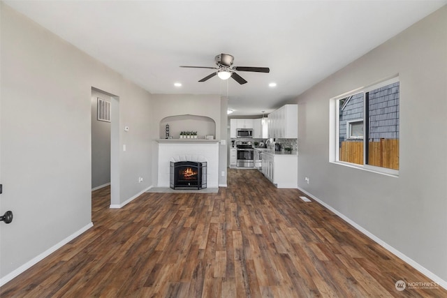 unfurnished living room with a fireplace with flush hearth, dark wood finished floors, recessed lighting, baseboards, and ceiling fan