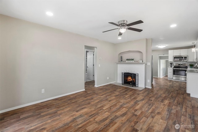 unfurnished living room with a ceiling fan, dark wood-style floors, recessed lighting, a fireplace, and baseboards