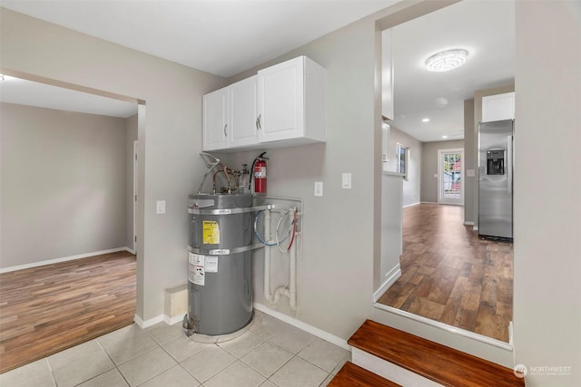 interior space with water heater, white cabinets, stainless steel fridge with ice dispenser, light tile patterned floors, and baseboards