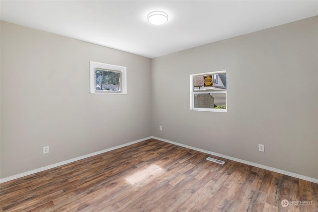 empty room with wood finished floors, visible vents, and baseboards