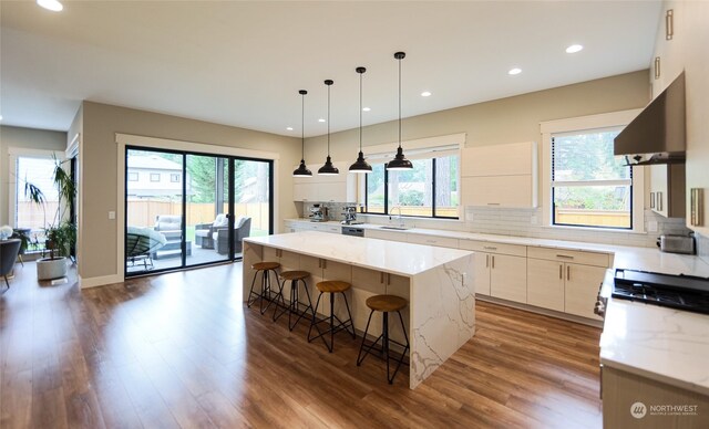 kitchen with hardwood / wood-style floors, a kitchen island, light stone counters, and extractor fan