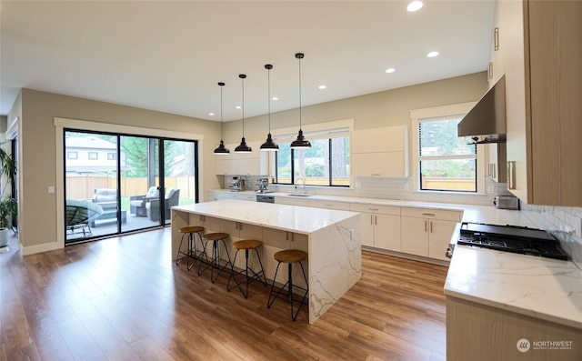 kitchen with a kitchen island, exhaust hood, light stone countertops, sink, and light wood-type flooring