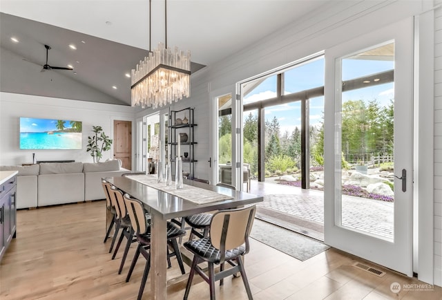 dining area featuring ceiling fan with notable chandelier, vaulted ceiling, and light hardwood / wood-style flooring