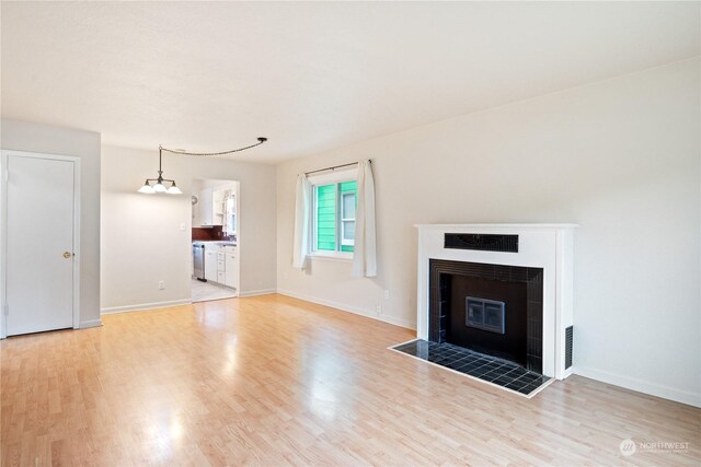 unfurnished living room featuring light wood-type flooring, a tiled fireplace, and a chandelier