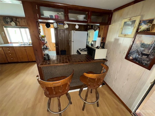 kitchen featuring glass insert cabinets, light wood-type flooring, white appliances, and wood walls