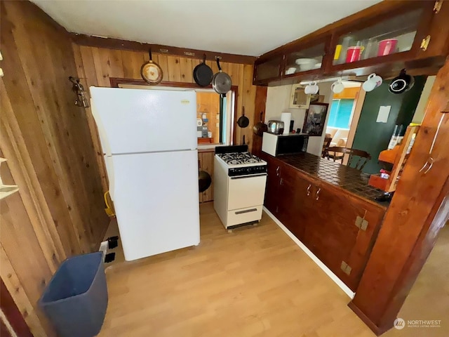 kitchen with wood walls, white appliances, light wood-type flooring, and tile counters
