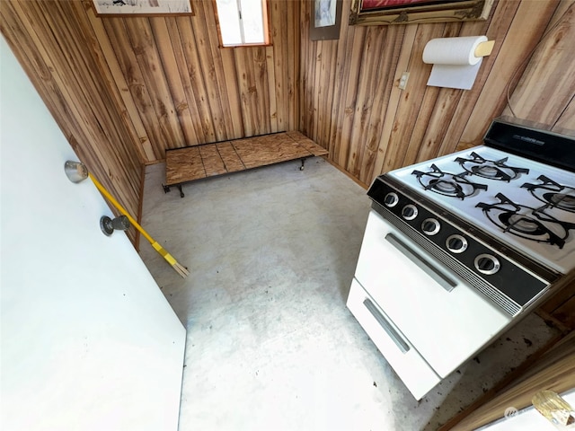 room details featuring concrete flooring, wooden walls, and white range with gas cooktop