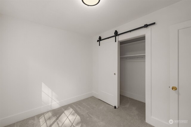 unfurnished bedroom featuring light carpet, a barn door, and a closet