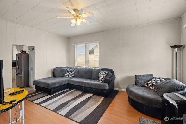 living room with ceiling fan, wooden walls, and wood-type flooring