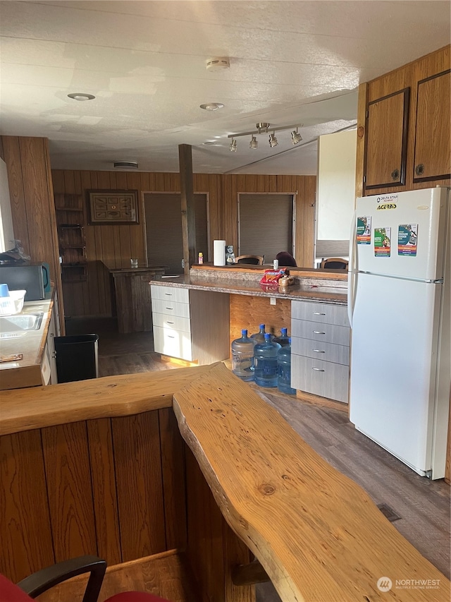 kitchen featuring dark wood-type flooring, kitchen peninsula, white fridge, and wooden walls