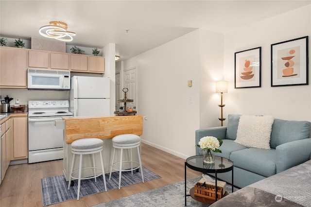 kitchen with a kitchen bar, white appliances, light hardwood / wood-style flooring, and light brown cabinetry