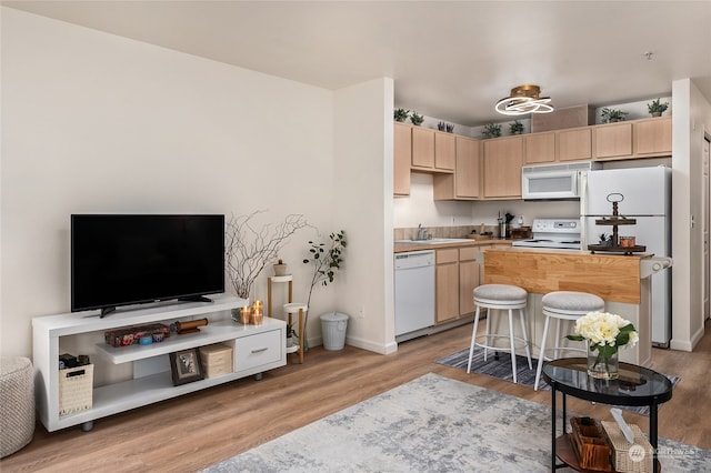 kitchen featuring white appliances, light hardwood / wood-style flooring, a kitchen bar, sink, and light brown cabinets