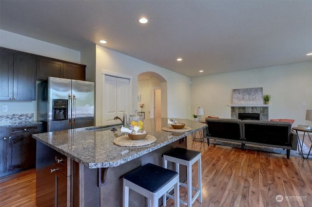 kitchen with hardwood / wood-style floors, stainless steel fridge, a tile fireplace, sink, and a center island with sink