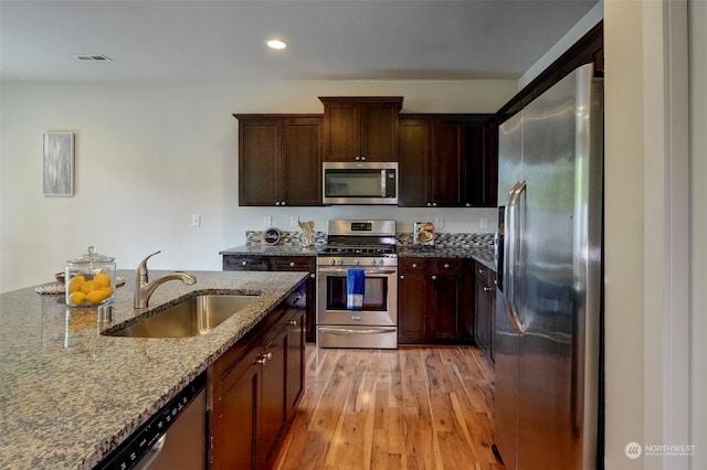 kitchen featuring light wood-type flooring, appliances with stainless steel finishes, stone countertops, and sink