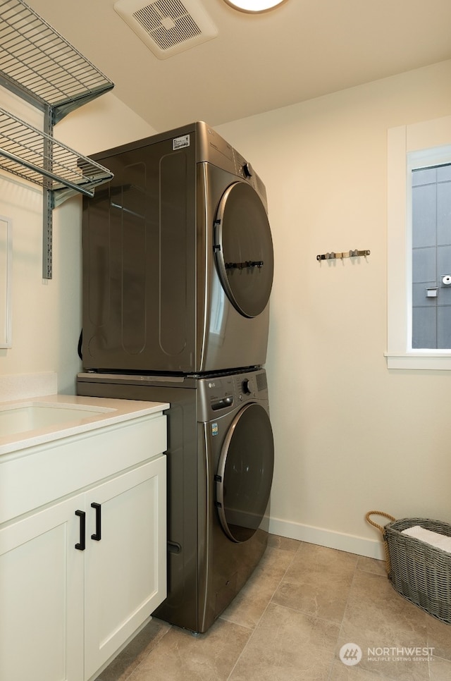 washroom with cabinets, light tile patterned floors, and stacked washing maching and dryer