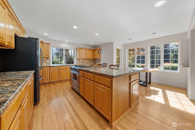 kitchen featuring appliances with stainless steel finishes, light wood-type flooring, an island with sink, and a wealth of natural light