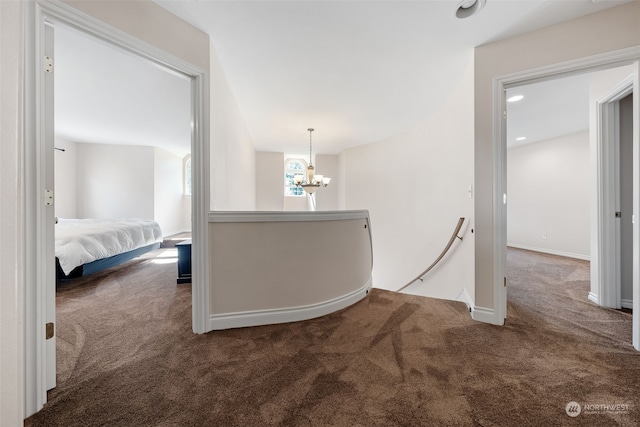 hall with a chandelier and dark colored carpet