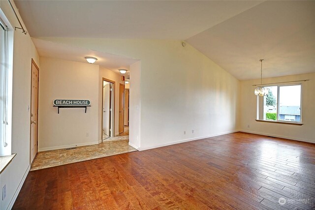 spare room featuring an inviting chandelier, lofted ceiling, and hardwood / wood-style flooring