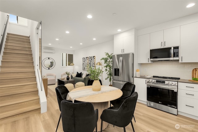 kitchen featuring a wall mounted air conditioner, backsplash, white cabinets, light hardwood / wood-style flooring, and stainless steel appliances