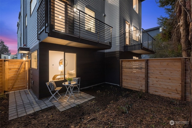 back house at dusk featuring a balcony and a patio area