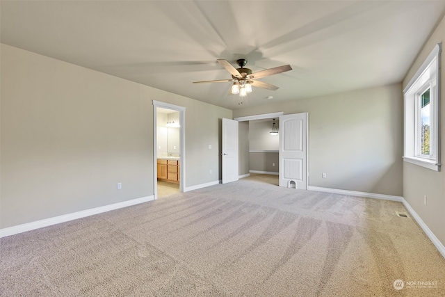 unfurnished bedroom featuring ceiling fan, light carpet, and ensuite bath