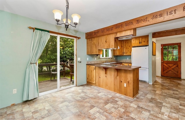 kitchen featuring hanging light fixtures, white refrigerator, kitchen peninsula, a breakfast bar area, and an inviting chandelier