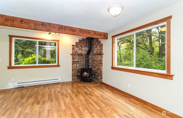 unfurnished living room with a baseboard radiator, a wood stove, light hardwood / wood-style floors, and a wealth of natural light