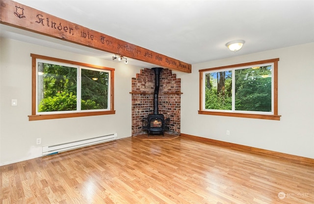 unfurnished living room with light hardwood / wood-style flooring, a wood stove, and a baseboard heating unit