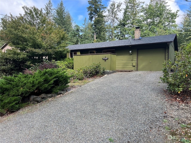 exterior space featuring a garage, driveway, a shingled roof, and a chimney