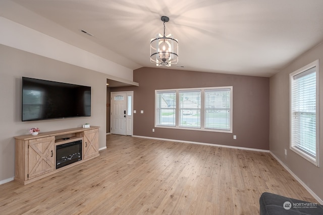 unfurnished living room featuring a chandelier, light wood-type flooring, vaulted ceiling, and a wealth of natural light