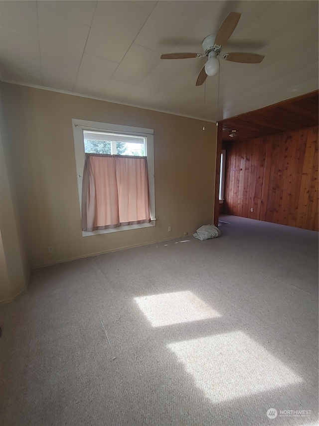 carpeted spare room with ceiling fan and wood walls