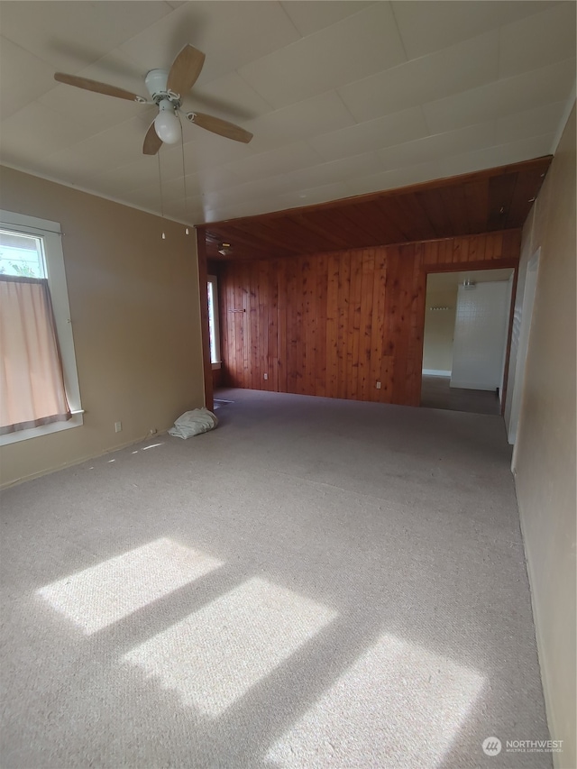 unfurnished room featuring wooden walls, ceiling fan, and carpet floors