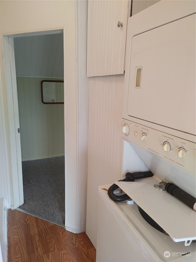 laundry area with wood walls, stacked washer and clothes dryer, and hardwood / wood-style flooring