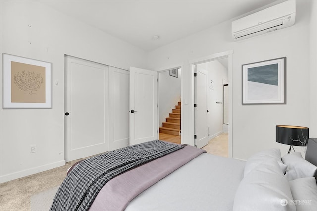 bedroom featuring light carpet, a closet, ensuite bath, and a wall mounted air conditioner