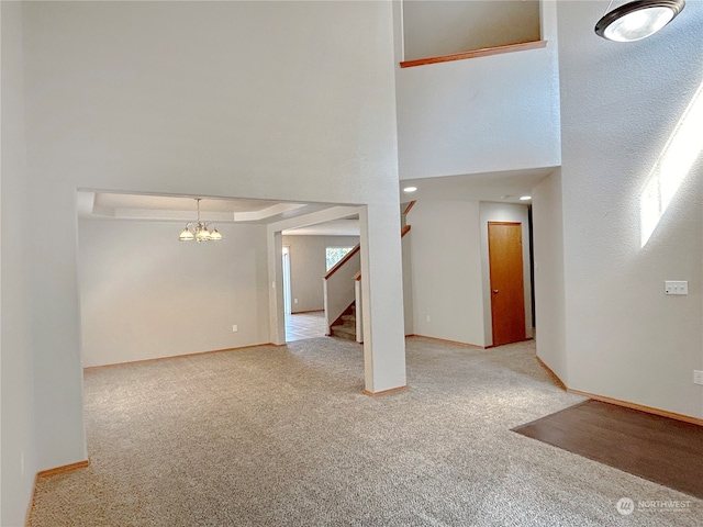 carpeted empty room featuring a notable chandelier and a high ceiling