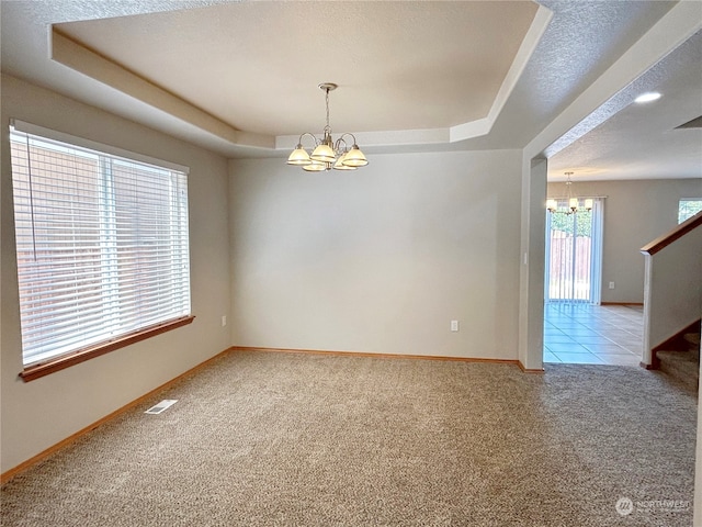 carpeted empty room with a raised ceiling, a chandelier, and a textured ceiling