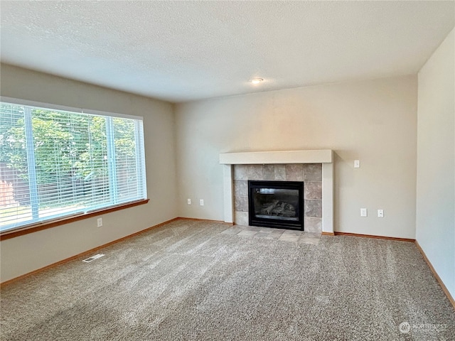 unfurnished living room with light colored carpet, a tile fireplace, and a textured ceiling