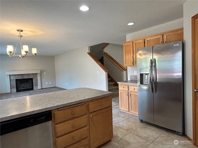 kitchen featuring a tile fireplace, decorative light fixtures, stainless steel appliances, a notable chandelier, and a textured ceiling