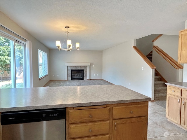 kitchen featuring a textured ceiling, a tile fireplace, an inviting chandelier, hanging light fixtures, and stainless steel dishwasher