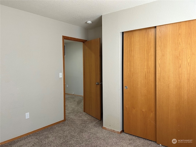 unfurnished bedroom with a textured ceiling, carpet floors, and a closet