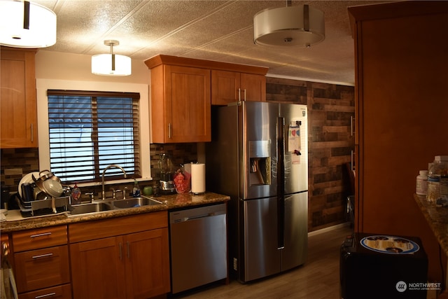 kitchen featuring pendant lighting, wood walls, sink, appliances with stainless steel finishes, and hardwood / wood-style flooring