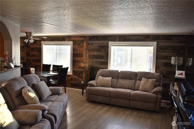 living room with a wealth of natural light, ceiling fan, wood walls, and hardwood / wood-style floors