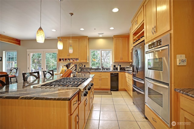 kitchen with a center island with sink, hanging light fixtures, appliances with stainless steel finishes, and dark stone counters