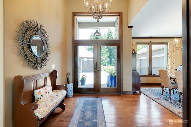 foyer with a towering ceiling, an inviting chandelier, french doors, and hardwood / wood-style flooring