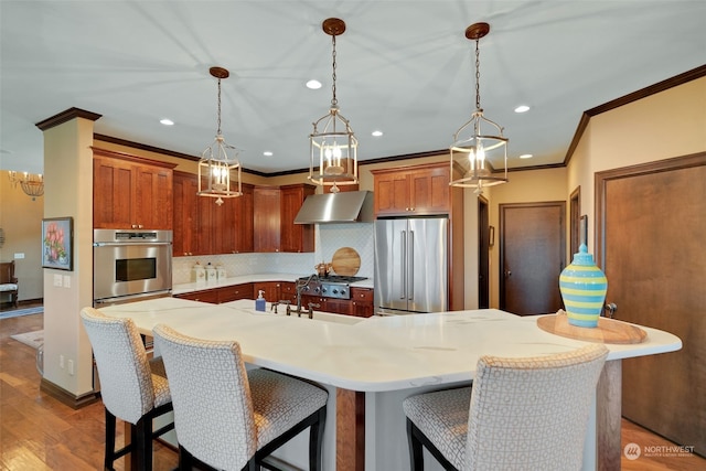 kitchen with decorative light fixtures, wall chimney exhaust hood, appliances with stainless steel finishes, a kitchen bar, and dark hardwood / wood-style flooring