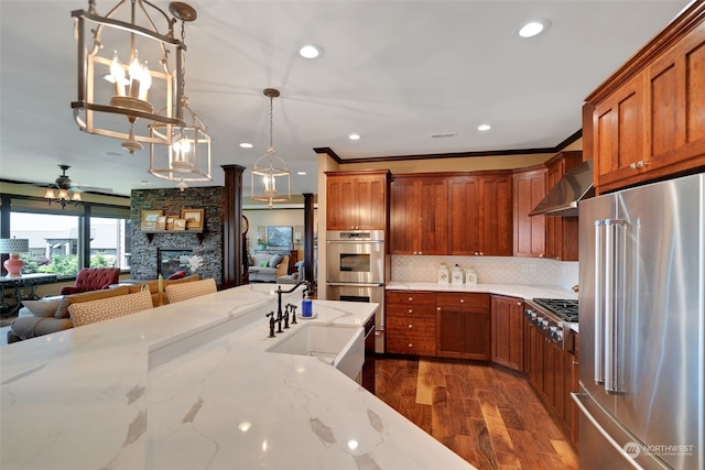 kitchen featuring pendant lighting, light stone counters, dark wood-type flooring, a fireplace, and appliances with stainless steel finishes